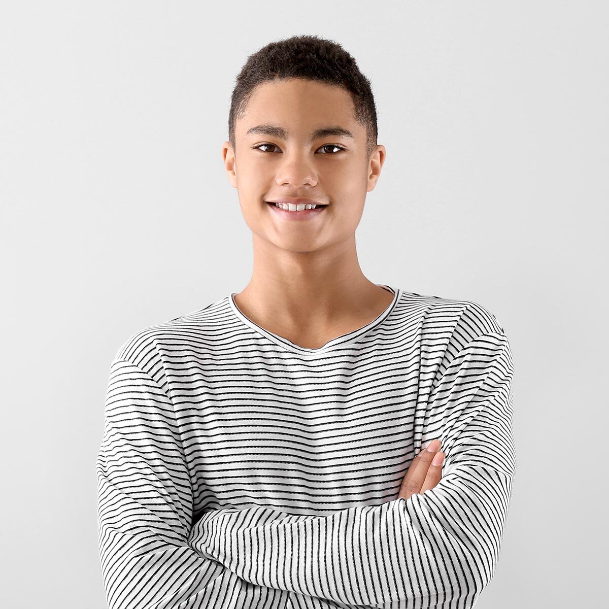Teenage boy with short hair smiling in a striped long-sleeve shirt, arms crossed.