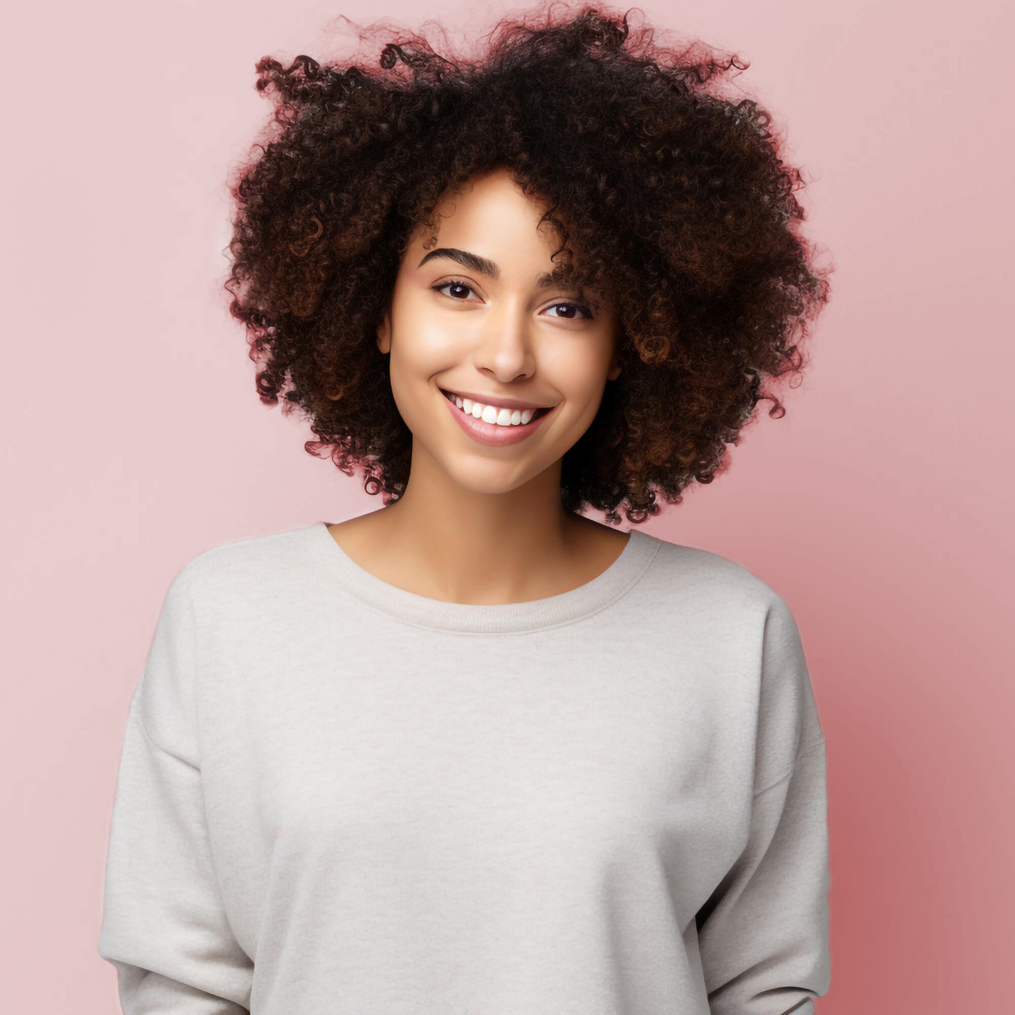 Young woman with curly hair wearing a light gray sweater on a pink background.
